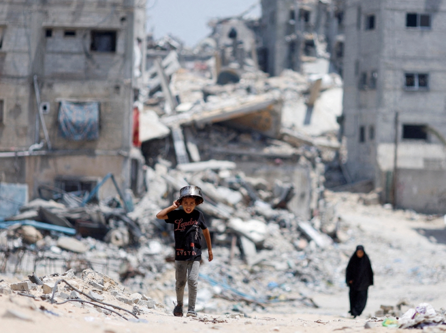 (FILE PHOTO) Palestinians walk by houses which were destroyed in an Israeli strike. (REUTERS/Mohammed Salem/File Photo)