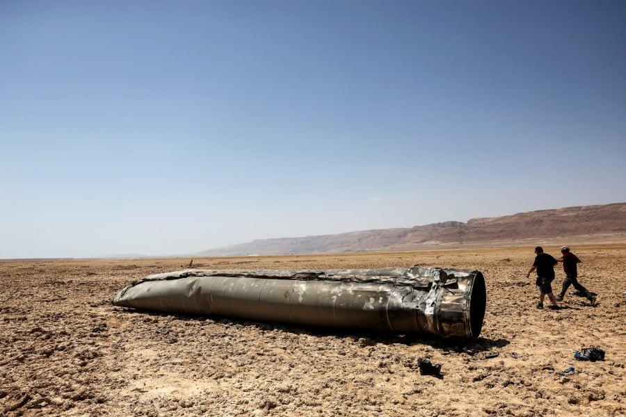 People walk next to the apparent remains of a ballistic missile, in the desert near the Dead Sea, following a massive missile and drone attack by Iran on Israel, in southern Israel. (REUTERS/Ronen Zvulun)