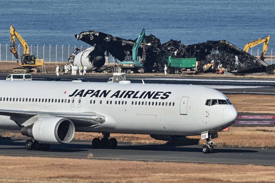A Japan Airlines (JAL) plane taxis past as officials remove the remaining debris (behind) of a JAL passenger plane from the runway area at Tokyo International Airport at Haneda on January 5, 2024. AFP PIC