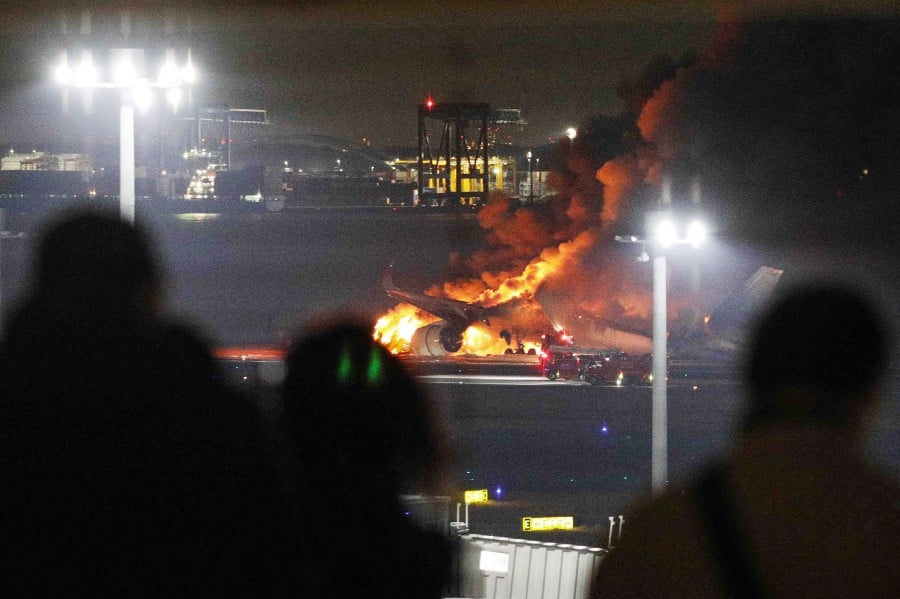 This photo provided by Jiji Press shows people on an observation deck looking at a Japan Airlines plane on fire on a runway of Tokyo's Haneda Airport. A Japan Airlines plane burst into flames on the runway of Tokyo's Haneda Airport on January 2 after apparently colliding with a coast guard aircraft, media reports said. (Photo by JIJI PRESS / AFP) 