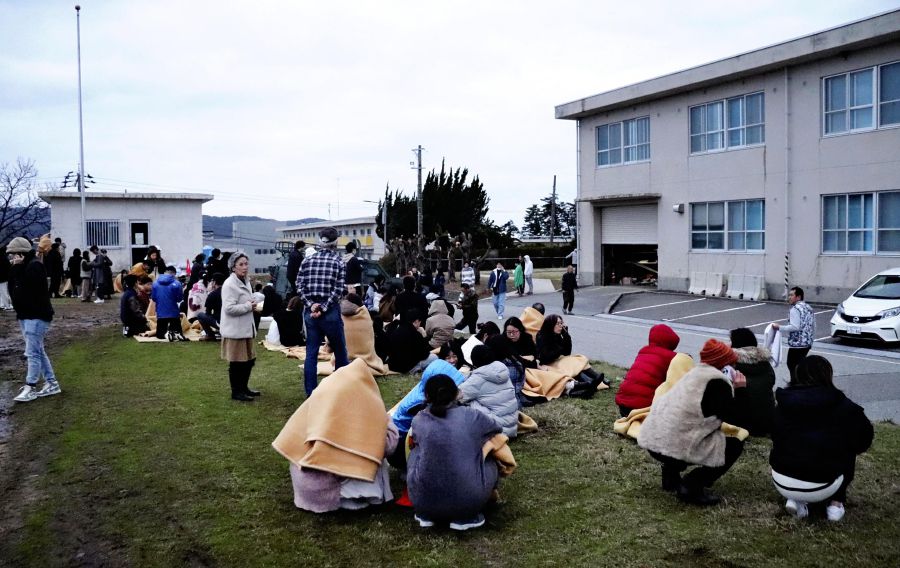 People sit outside in the open after evacuating from buildings in the city of Wajima, Ishikawa prefecture on January 1, 2024, after a major 7.5 magnitude earthquake struck the Noto region in Ishikawa prefecture in the afternoon. Tsunami waves over a metre high hit central Japan on January 1 after a series of powerful earthquakes that damaged homes, closed highways and prompted authorities to urge people to run to higher ground. (Photo by Yusuke FUKUHARA / Yomiuri Shimbun / AFP) 