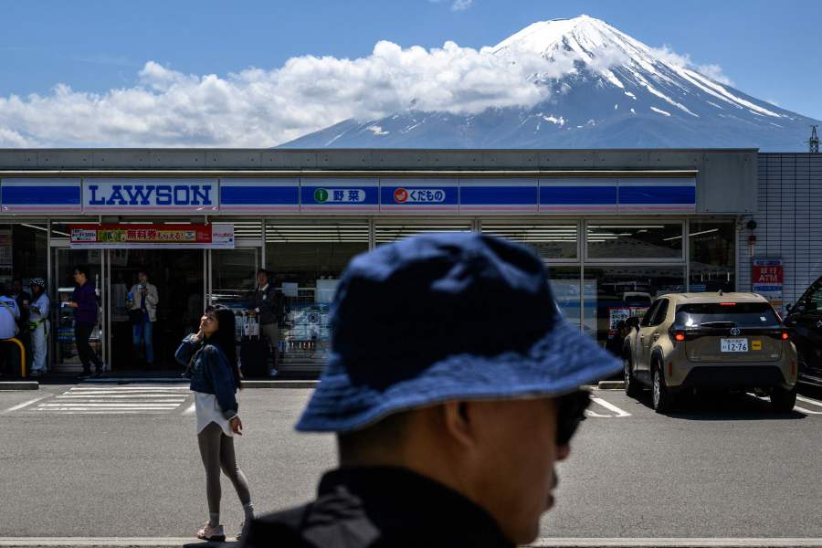 A tourist poses in front of a convenience store with Mount Fuji, before a huge black barrier which will be installed to block Mount Fuji from view, in the town of Fujikawaguchiko, Yamanashi prefecture. - AFP pic