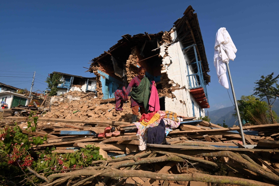 A survivor searches for belongings through the ruins of her damaged house in Khalanga of Jajarkot district. (Photo by PRAKASH MATHEMA / AFP)
