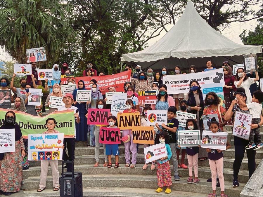 Women and their stateless children holding up placards after a ‘yasin’ recital and ‘tahlil’ for the late Sabeena Syed Jafer on June 7 at Tasik Aman Jaya in Perak.