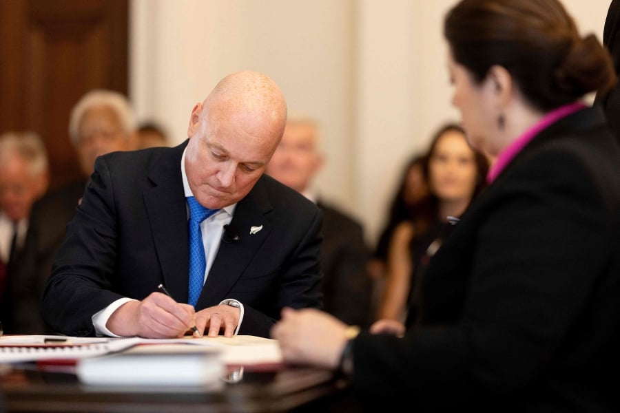 New Zealand's new Prime Minister Christopher Luxon (left) signs documents with New Zealand's Governor General Dame Cindy Kiro during the swearing-in of the new government at Government House in Wellington. (Photo by Marty MELVILLE / AFP)