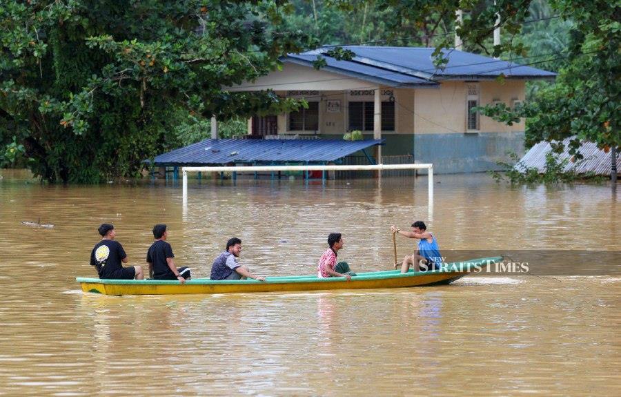 A group of young locals making their way through a flooded area with a boat in Kampung Manek Urai, Kuala Krai following the overflow of Sungai Lebir yesterday morning. - BERNAMA PIC