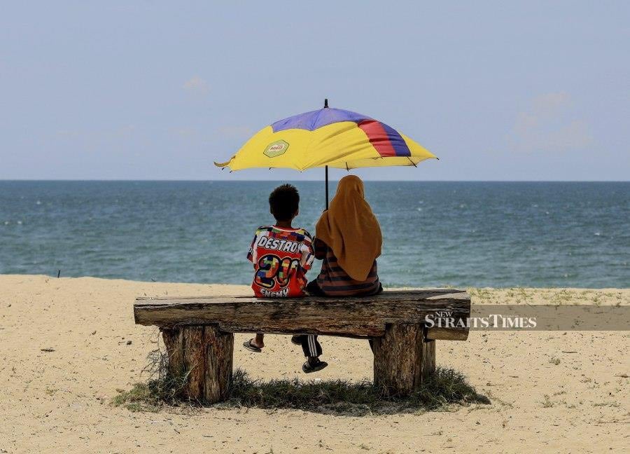 TERENGGANU: A mother and child using an umbrella to shield themselves from the hot weather at Batu Burok Beach. - NSTP/GHAZALI KORI 