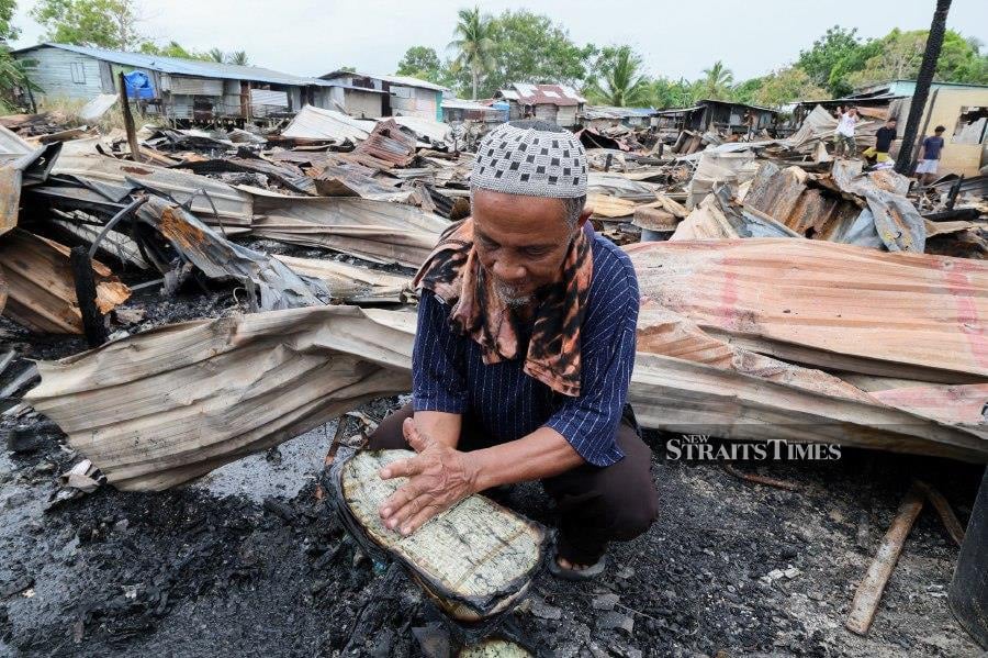 SANDAKAN: Ibnu Dammang, 70, cleaning a Quran nearly destroyed in a fire at the squatter area of Kampung Mangkalinau Parti, Sandakan. - BERNAMA PIC 