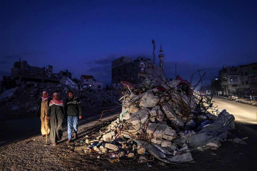 Vehicles light up a road as men walk past the rubble of a building destroyed by Israeli bombardment in Rafah in the southern Gaza Strip. (Photo by Mohammed ABED / AFP)