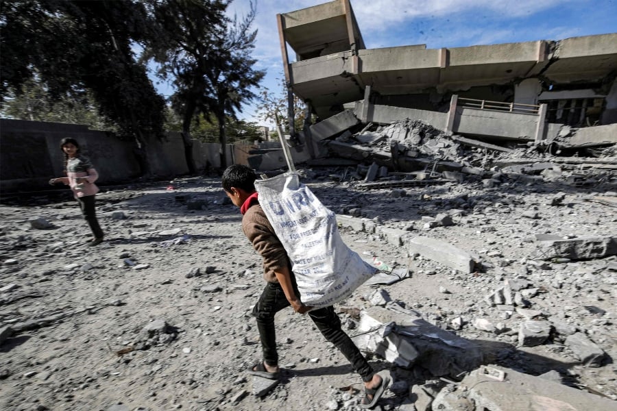A boy carries a sack bearing the logo of the United Nations Relief and Works Agency for Palestine Refugees in the Near East (UNRWA), filled with salvaged items from the rubble of a destroyed highschool in the Nuseirat camp for Palestinian refugees. (Photo by ANAS BABA / AFP)