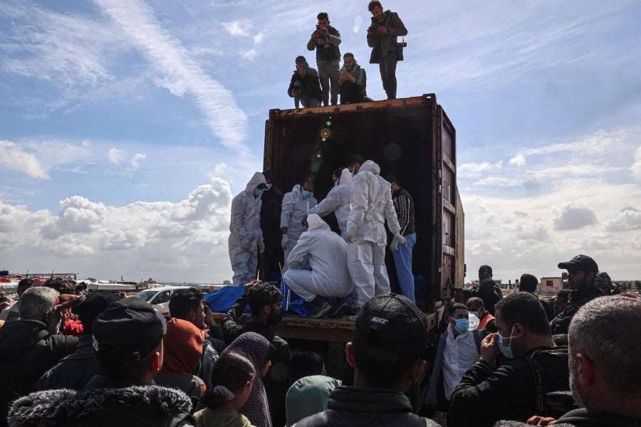 Men in white hazmat suits aligned the bodies wrapped in blue plastic sheeting at the bottom of a trench, before a bulldozer covered them in sand as dozens of mourners looked on. (Photo by SAID KHATIB / AFP)