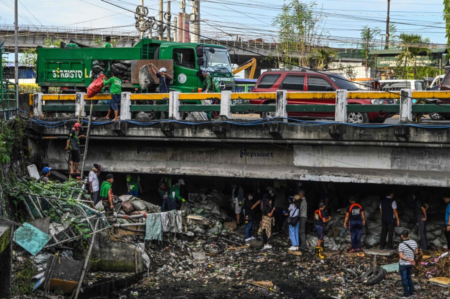 In this photo taken on December 21, 2023 government workers pick up trash under a bridge in Paranaque, Metro Manila. Inadequate garbage collection services, lack of disposal and recycling facilities, and grinding poverty have been blamed for the growing problem of plastic waste across the Philippines. AFP