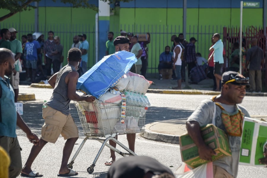 A man pushes a shopping trolley on the street as crowds leave shops with looted goods amid a state of unrest in Port Moresby. (Photo by AFP)