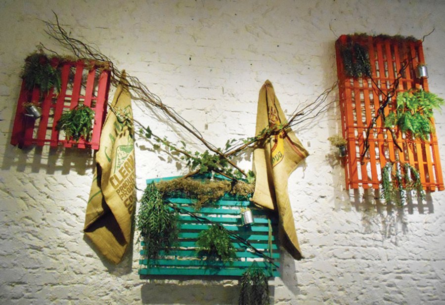 A combination of dried twigs and natural-looking fake leaves against vivid wooden strips make an eye-catching display. Additional elements are the cloth bags hung from nails on the wall.