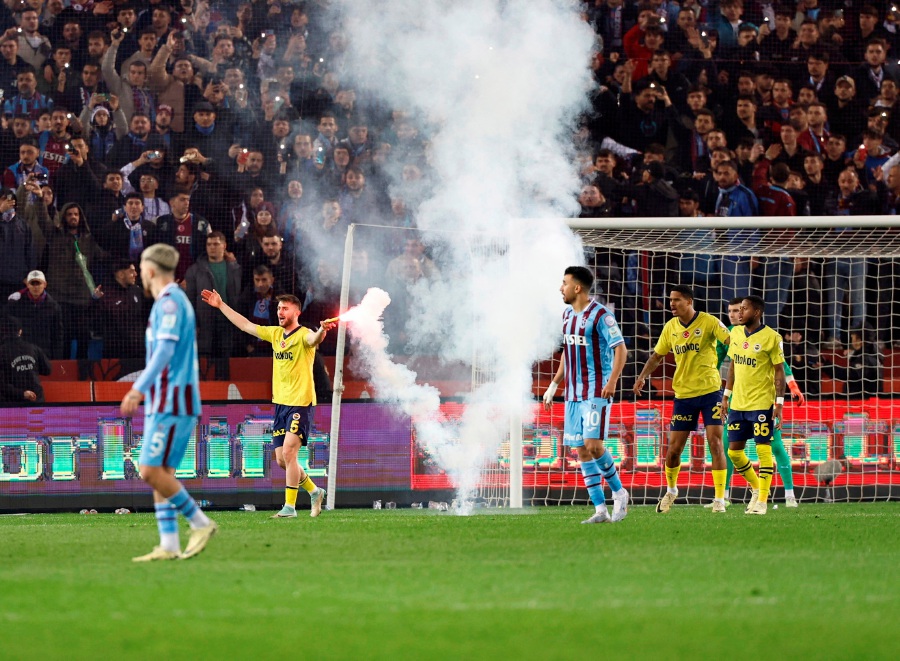 Fenerbahce's Ismail Yuksek holds a flare thrown by Trabzonspor fans.- REUTERS PIC