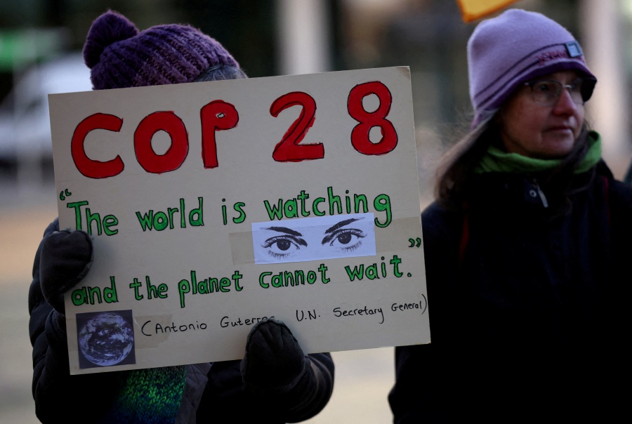 A climate activist holds a placard during a vigil to mark the opening day of the COP28 summit outside the offices of the BBC in Salford, Britain, November 30, 2023. - REUTERS Pic