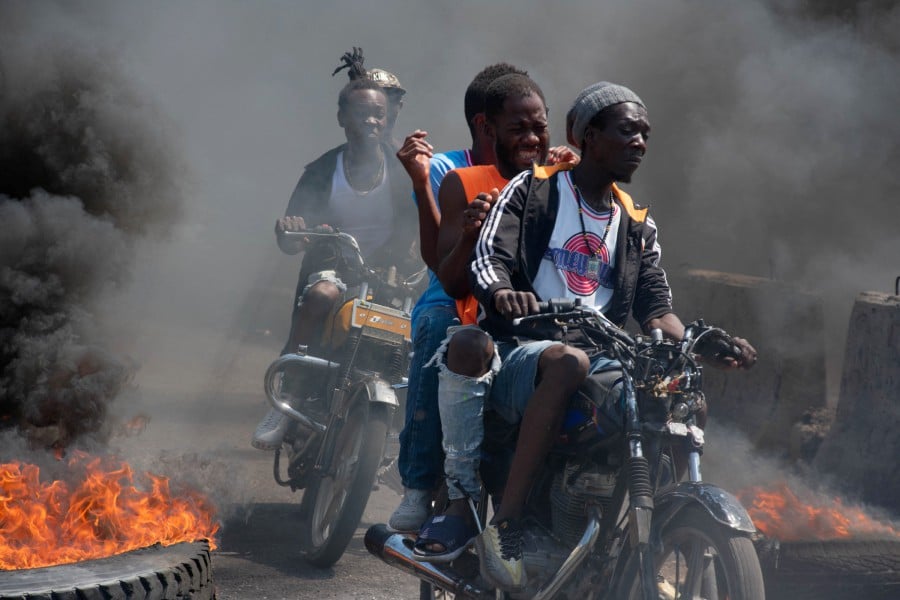 Men on motorcycles riding past burning tires during a demonstration following the resignation of its Prime Minister Ariel Henry, in Port-au-Prince, Haiti, on March 12, 2024. -- AFP