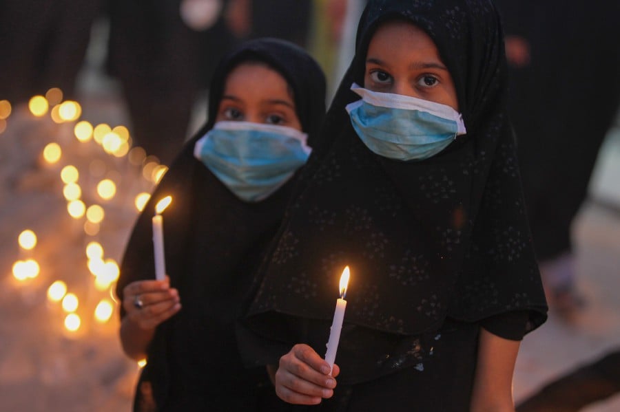 Iraqi girls, wearing protective face masks, carry candles during a memorial ceremony on the tenth day of the month of Muharram which marks the peak of Ashura, in the holy city of Karbala, on August 30, 2020. - Ashura is a period of mourning in remembrance of the seventh-century martyrdom Imam Hussein, who was killed in the battle of Karbala in modern-day Iraq, in 680 AD. (Photo by AHMAD AL-RUBAYE / AFP)