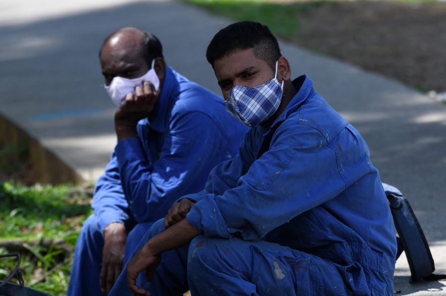 Workers wearing face masks, as a preventive measure against the spread of the COVID-19 coronavirus, wait for transport to their job sites in Singapore on April 15, 2020. - Singapore won praise for keeping its outbreak in check in the early stages of the fight against the COVID-19 novel coronavirus but has seen a surge in cases this month, with many linked to foreign workers' dormitories. (Photo by ROSLAN RAHMAN / AFP)