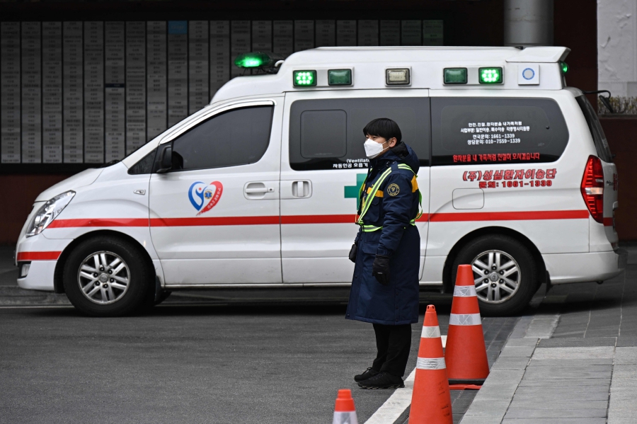 A parking attendant stands next to an ambulance outside a hospital in Seoul. (Photo by ANTHONY WALLACE / AFP)