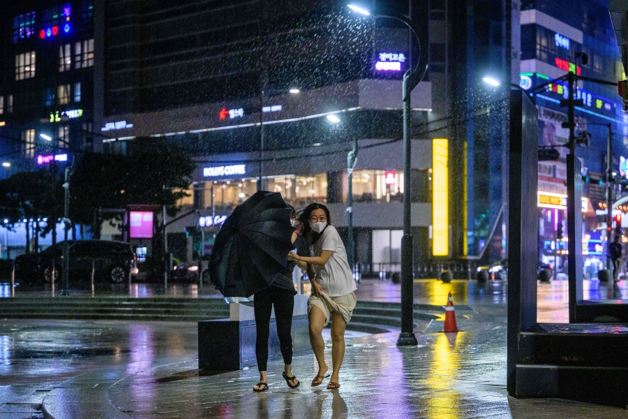 Pedestrians walk near a beach during a downpour as Typhoon Hinnamnor approaches in Busan. (Photo by Anthony WALLACE / AFP)