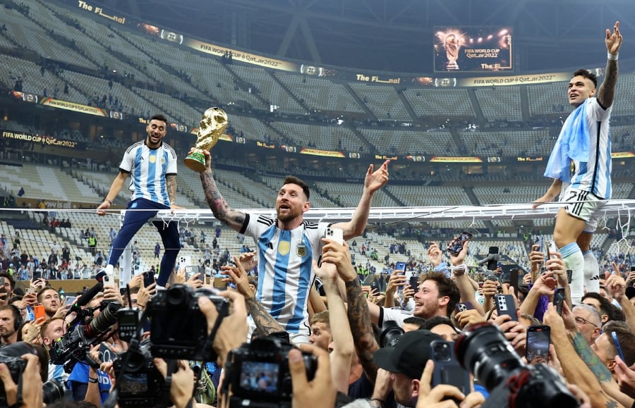 Argentina's Lionel Messi celebrates with the trophy after winning the World Cup as Lautaro Martinez is sat atop the frame of a goal. (REUTERS/Kai Pfaffenbach)
