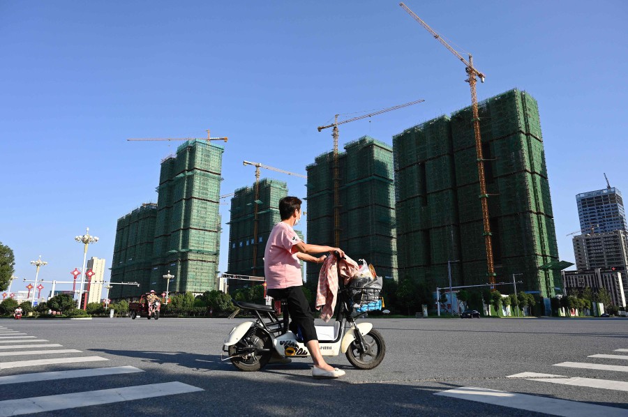TOPSHOT - A woman rides a scooter past the construction site of an Evergrande housing complex in Zhumadian, central China�s Henan province on September 14, 2021. (Photo by JADE GAO / AFP)