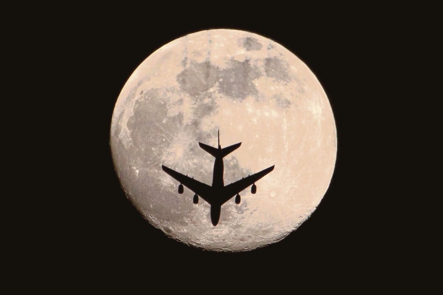 (FILE PHOTO) An aeroplane is pictured against the almost full "Pink Moon". -AFP/Hussein FALEH