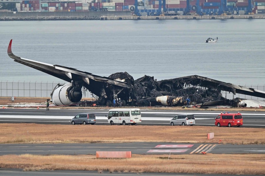 Officials look at the burnt wreckage of a Japan Airlines (JAL) passenger plane on the tarmac at Tokyo International Airport at Haneda in Tokyo on January 3, 2024, the morning after the JAL airliner hit a smaller coast guard plane on the ground. AFP PIC