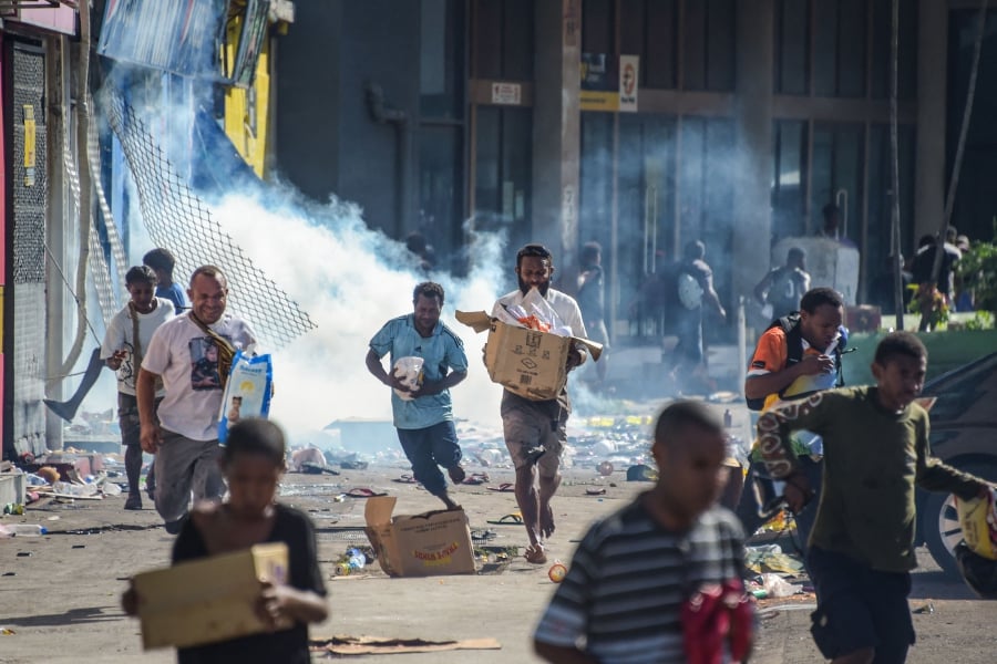 People run with merchandise as crowds leave shops with looted goods amid a state of unrest in Port Moresby. (Photo by AFP)