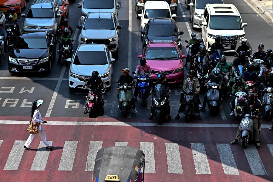 Motorcyclists wait under the shade as a woman crosses a traffic intersection in Bangkok. (Photo by MANAN VATSYAYANA / AFP)