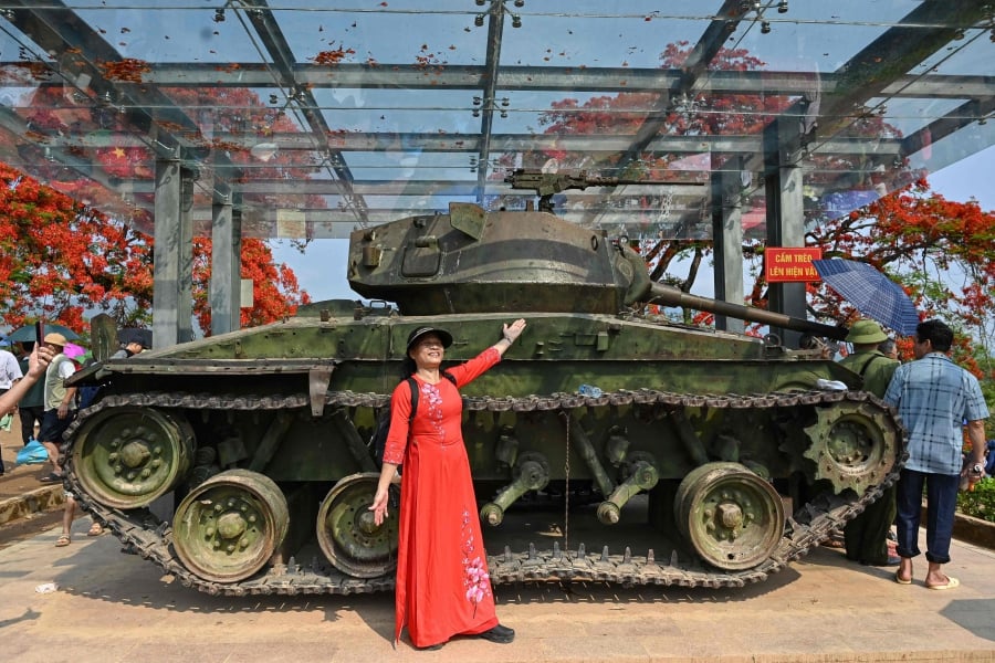A Vietnamese woman wearing a traditional dress poses for photos next to a French tank on top of A1 hill historical battle site in Dien Bien Phu city. (Photo by Nhac NGUYEN / AFP)