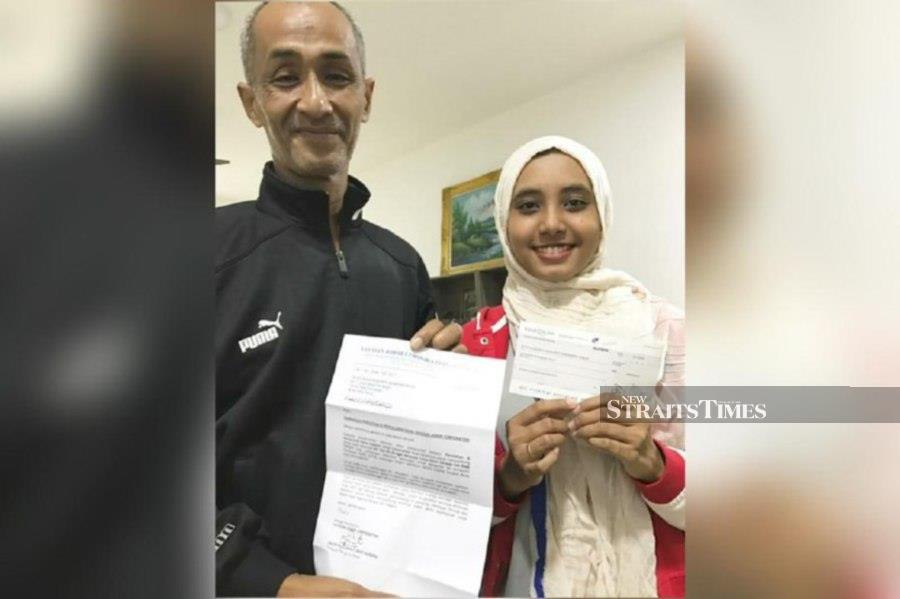 Nur Qistina Aiman Mohammed Amran (right) with her father receiving the Yayasan JCorp Early Educational Assistance for her admission into UiTM Melaka. - Pix by Vincent D’Silva 