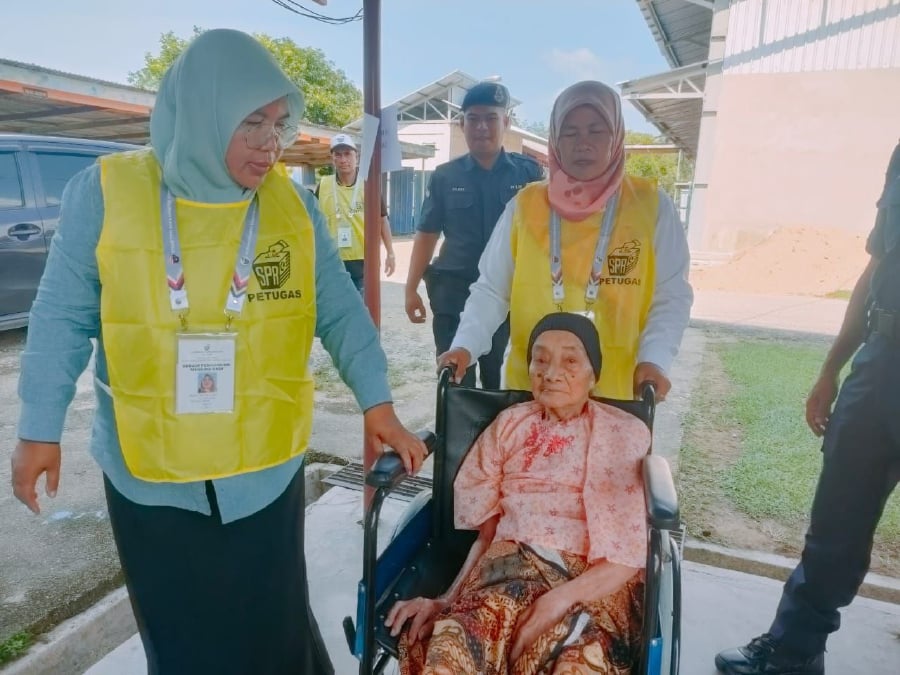 Munah Adam is helped by Election Commission personnel after arriving at the polling centre in SK Pasir Raja, Hulu Dungun -NSTP/ROSLI ILHAM