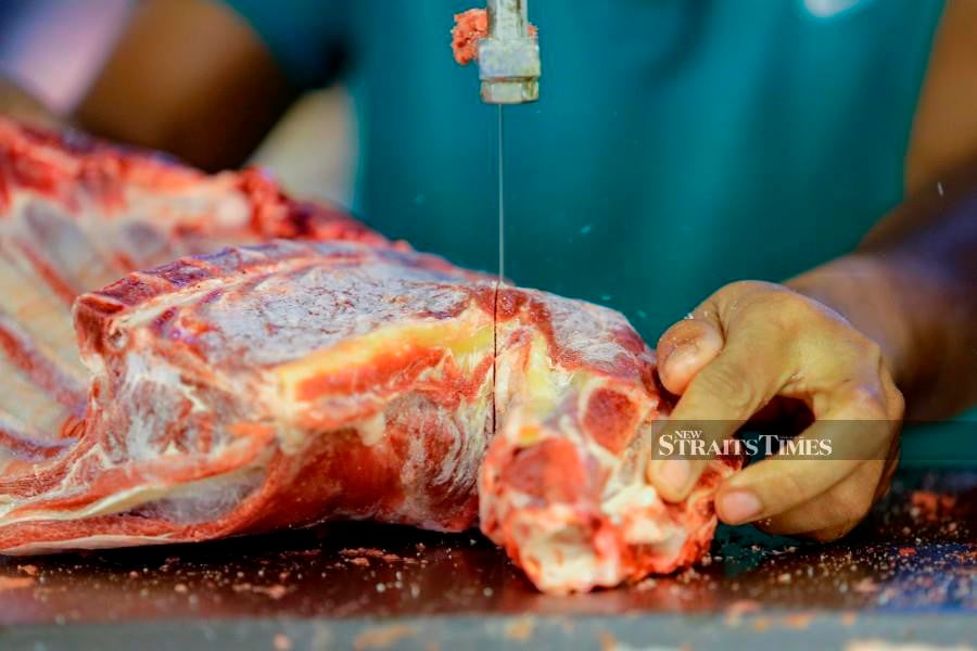 A worker at a market slices meat before the opening of market in Kuala Lumpur. -NSTP/AIZUDDIN SAAD