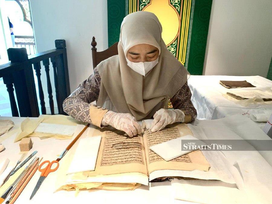 A Thai museum worker cleaning the old Quran exhibited at the museum. Pic by Sharifah Mahsinah Abdullah