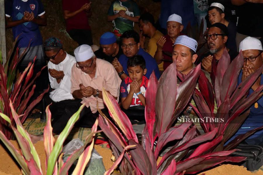 Attar Azim Syukran Jamil, 9, and other friends and relatives, praying for his parents and two younger siblings, all of whom were killed in a road crash in Jalan Kota Baru-Gua Musang, after their burial in the Felda Trolak Utara Muslim cemetery last night. NSTP/MUHAMAD LOKMAN KHAIRI
