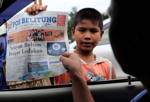 Wahyu Ardian, 10, earns extra income by selling copies of an Indonesian newspaper- Pos Belitung to a motorist in Belitung Island.AIZUDDIN SAAD