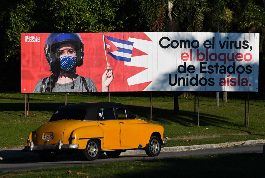 An old American car drives near a banner reading ‘As the virus, the United States blockade isolates’, in Havana, on January 31, 2021. - AFP PIC