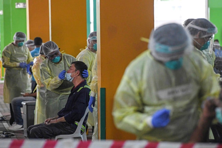 Health workers takes nasal swab test samples from essential workers to detect the COVID-19 novel coronavirus before the workers return to work in Singapore. -File pic via AFP