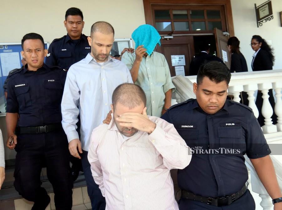 Policemen escort J. Balakrishnan (covering his face with a blue cloth), Seyed Mohsen Namazikivi Seyedreza (front left) and Mohammad Abbasi Younes (2nd-left, middle row) at the Penang High Court. -NSTP/Danial Saad