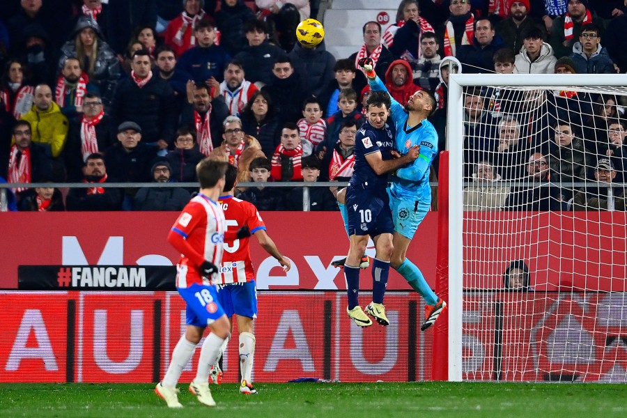 Real Sociedad's Spanish midfielder #10 Mikel Oyarzabal and Girona's Argentinian goalkeeper #13 Paulo Gazzaniga jump for the ball during the Spanish league football match between Girona FC and Real Sociedad at the Montilivi stadium in Girona on February 3, 2024. -- AFP