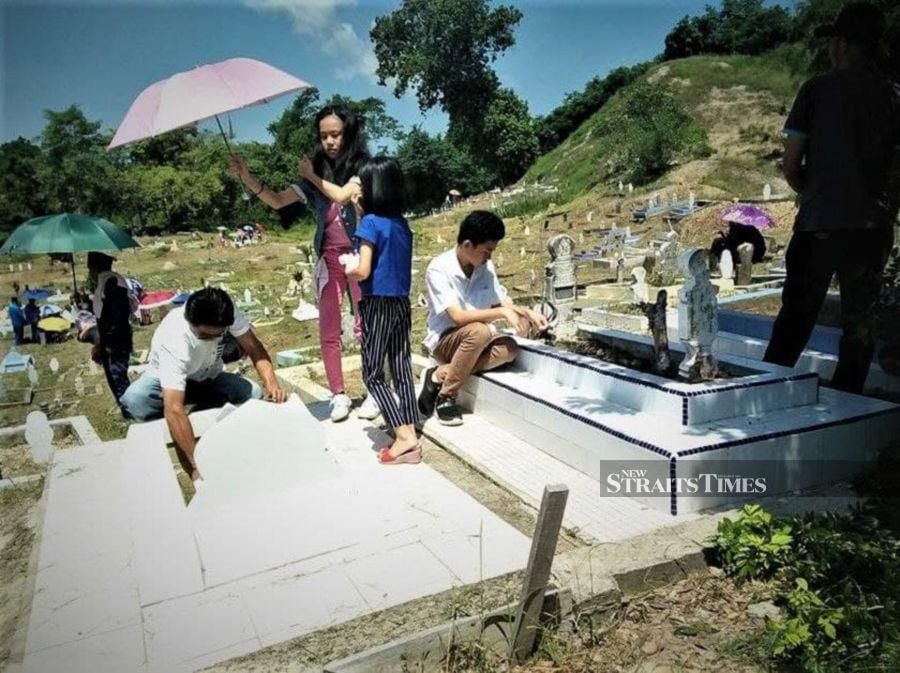 Volintine's family members cleaning up the graves of their Muslim grandparents. - NSTP/YUN MIKAIL