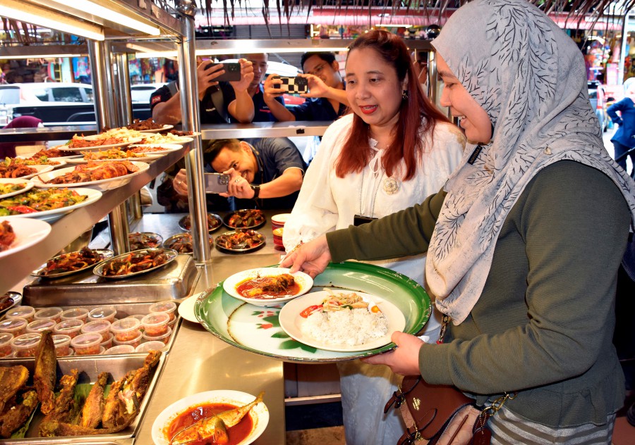  Melaka Domestic Trade and Cost of Living Ministry director Norena Jaafar (right) serving a customer at Restoran Asam Pedas Selera Kampung. - BERNAMA PIC