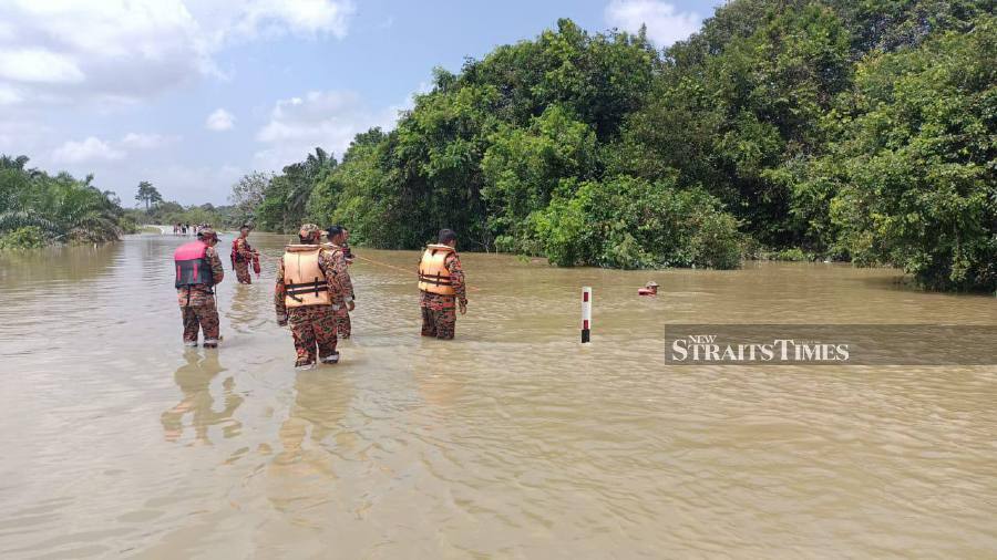 Firemen searching for the woman after the car she was travelling in was swept away by flood waters Jalan Nitar Utama, Mersing. - Pic courtesy of Fire and Rescue Dept.