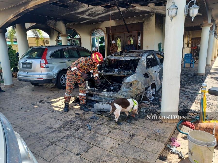 Firemen with a K9 tracker dog inspecting the burnt car at the home of Beruas MP, Datuk Ngeh Koo Ham at Lorong Semarak Jaya, Ayer Tawar, on Jan 10. - Pic courtesy of Fire and Rescue Dept. 