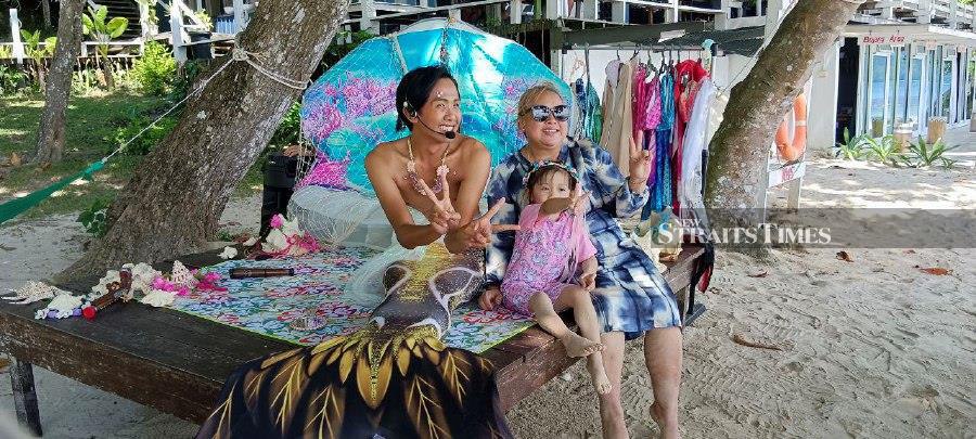 Nic Allen Jose or "Mermaid Nalu", 26, pose for a picture with island goers at the beach of Rainbow island, off Sepanggar. - NSTP/Olivia Miwil
