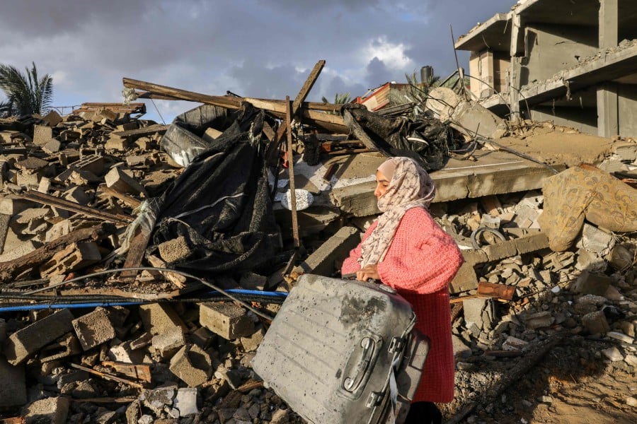 A Palestinian woman carries salvaged items on the rubble of buildings destroyed during Israeli strikes on Rafah. - AFP PIC
