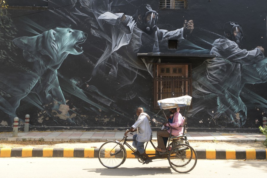 A rickshaw driver carries passengers wearing facemasks past a mural at Lodhi Art District during a government-imposed nationwide lockdown as a preventive measure against the COVID-19 coronavirus, in New Delhi. - AFP