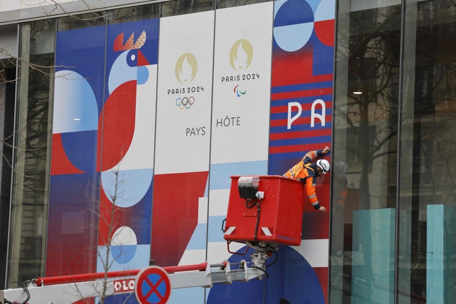Workers set up a giant poster announcing the Olympic Games on the facade of the Solidarity and Health ministry in Paris. - AFP PIC